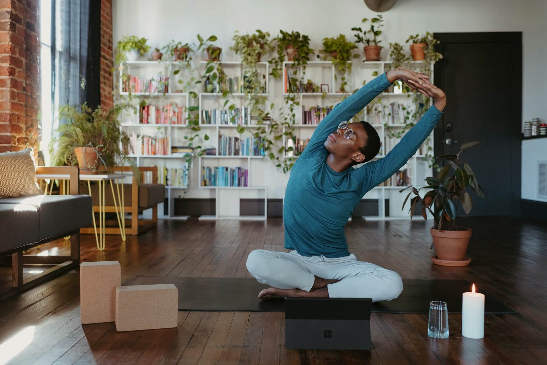 Person stretching on yoga mat with bookshelf and plants in background